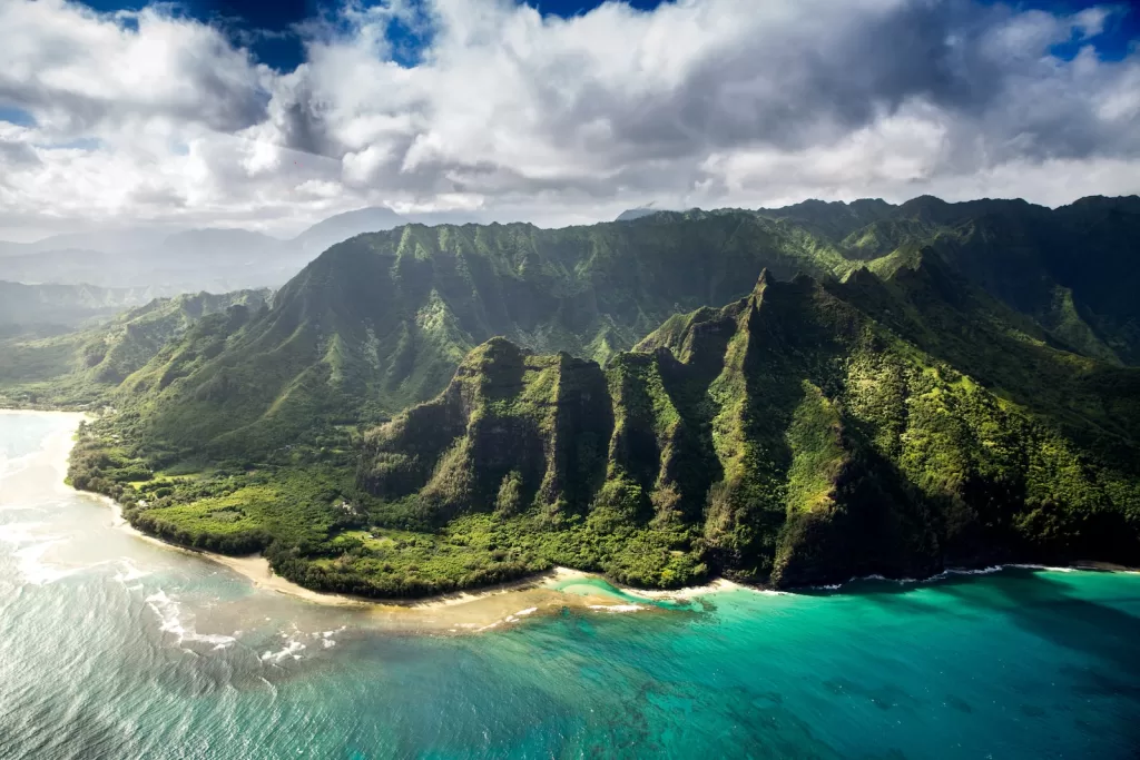least expensive time to travel to Hawaii, aerial photography of green mountain beside body of water under white sky